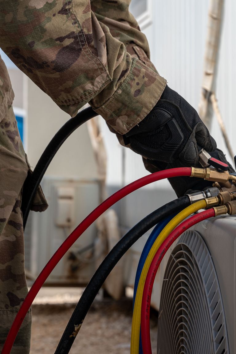 Technician connecting refrigerant gauge hoses to an outdoor air conditioning unit