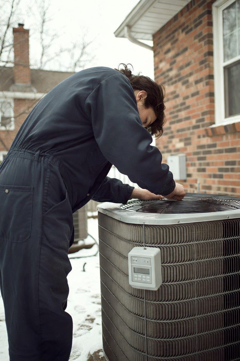 Technician inspecting a heat pump outdoor unit in winter snow
